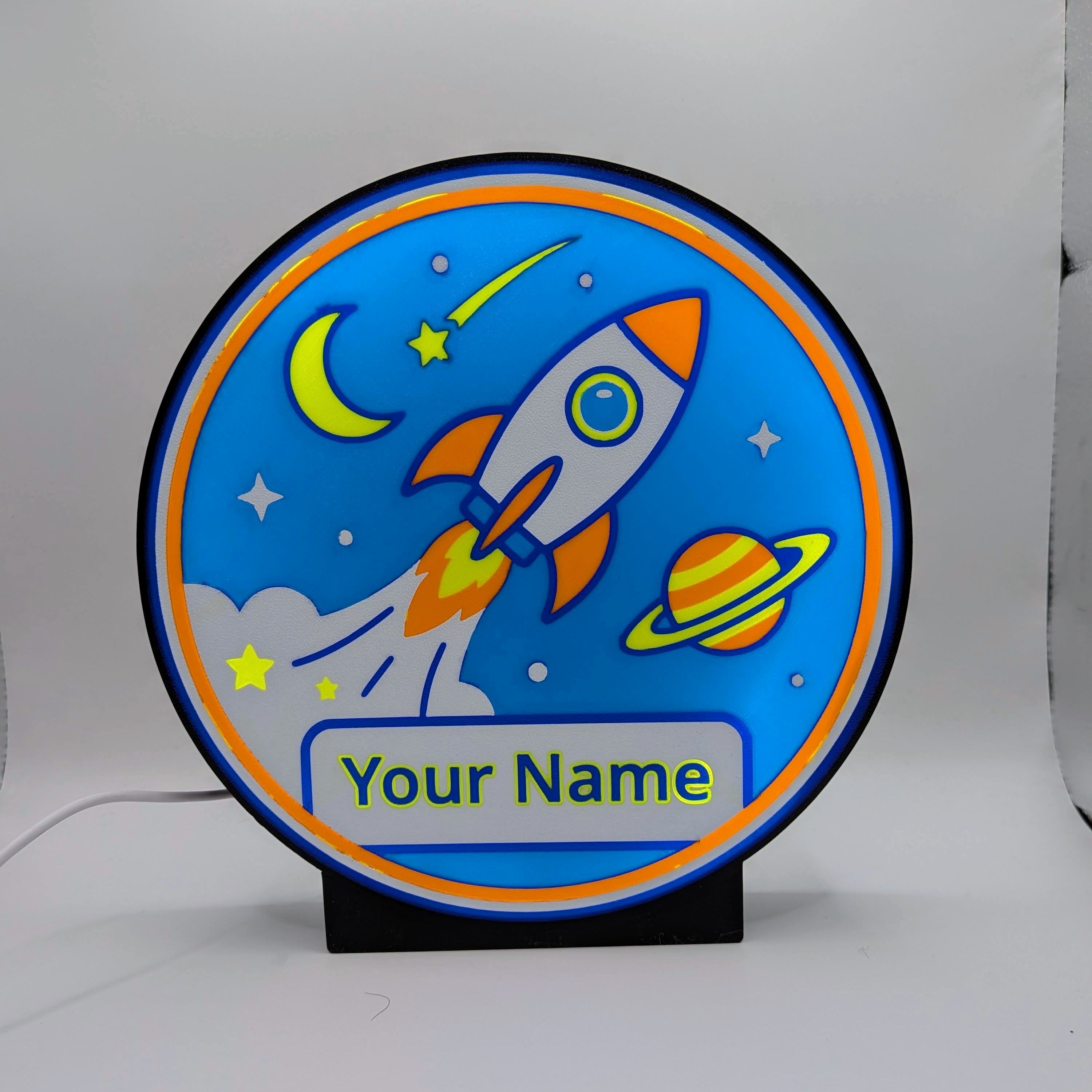 Lampada LED cameretta rotonda blu con razzo e scritta 'Your Name', su base nera