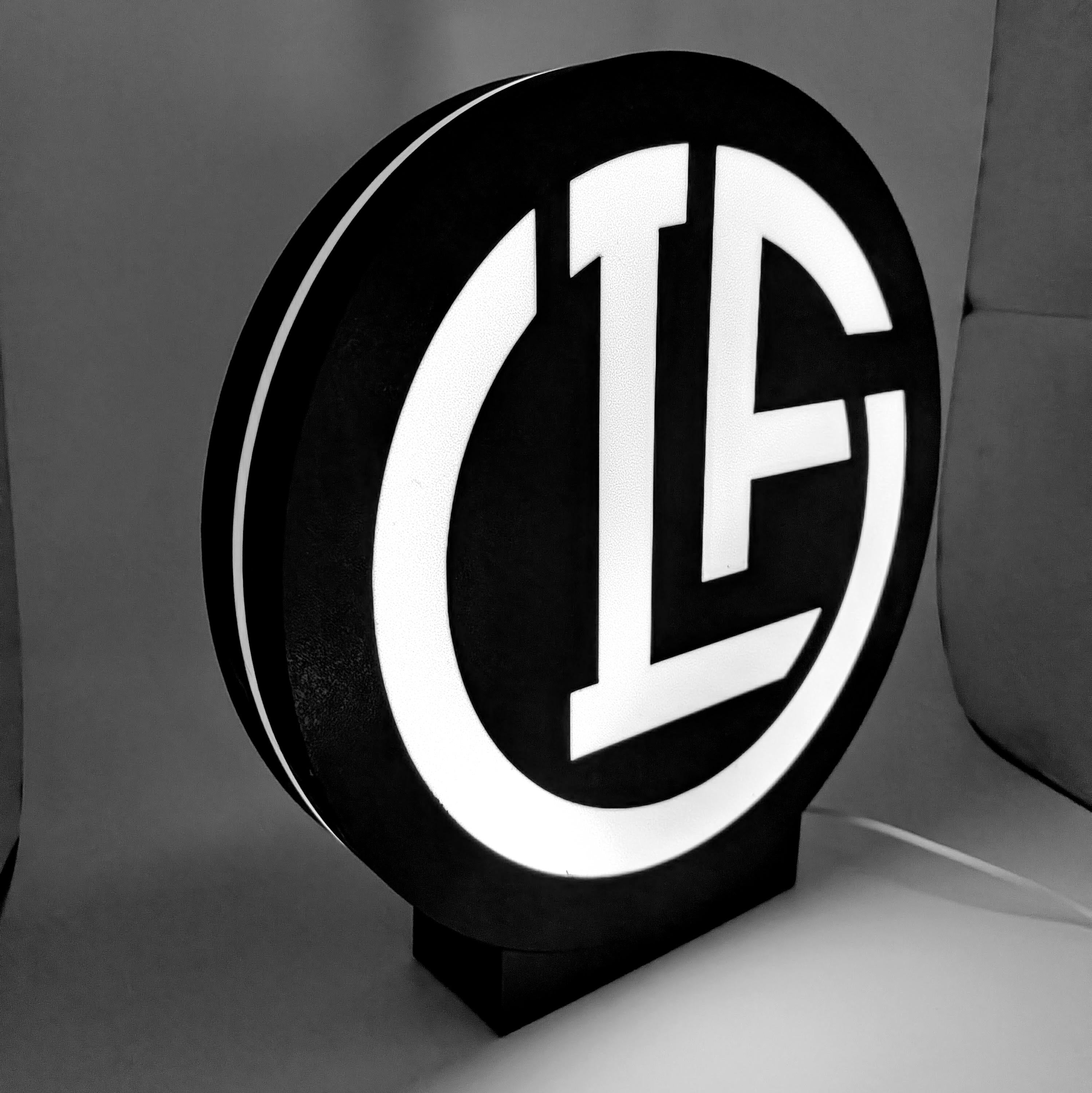 Black round LED lightbox with white circular emblem and block letters