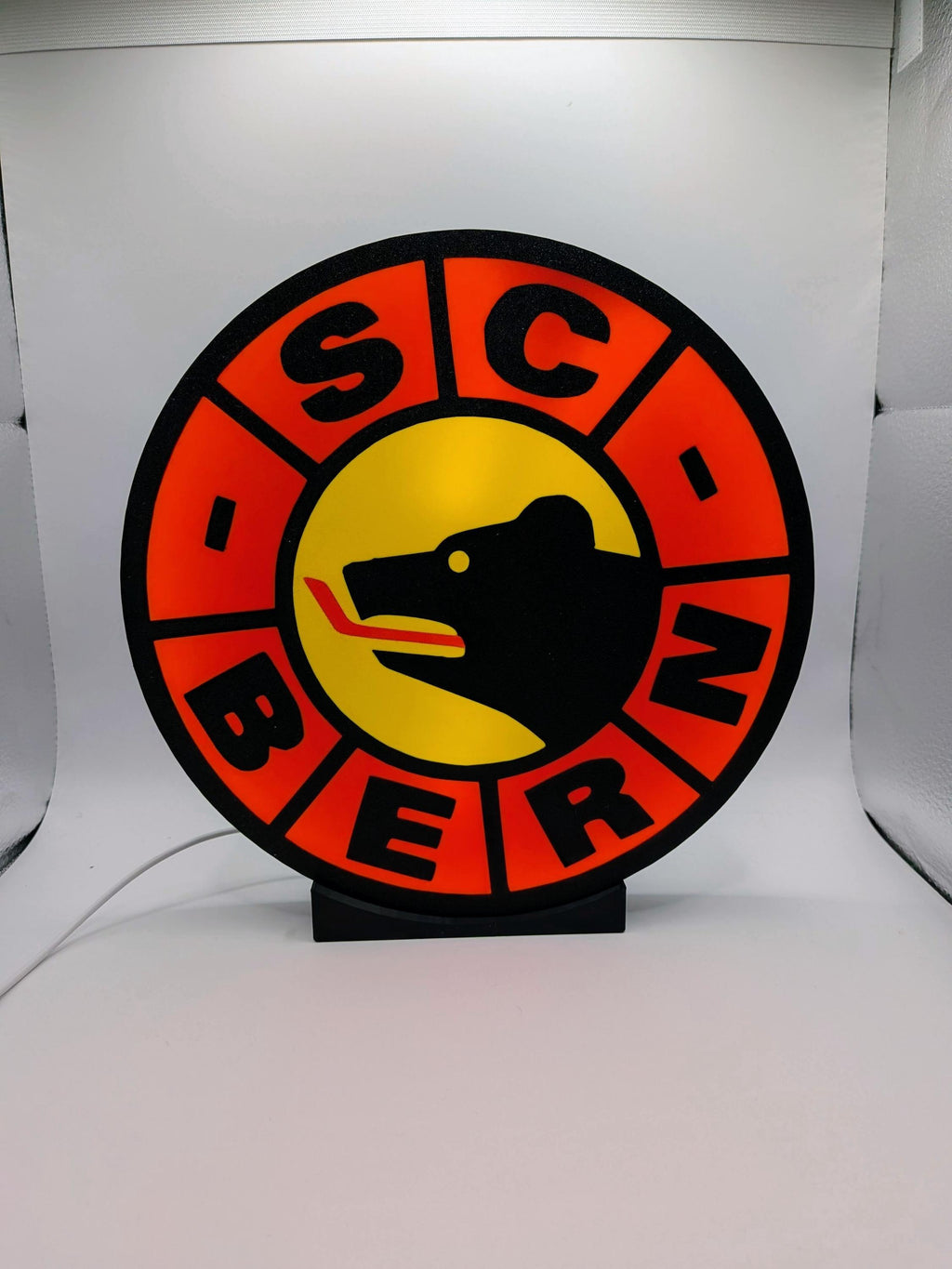 Lampada LED rotonda SC Bern su supporto nero, bordo arancione e centro giallo.