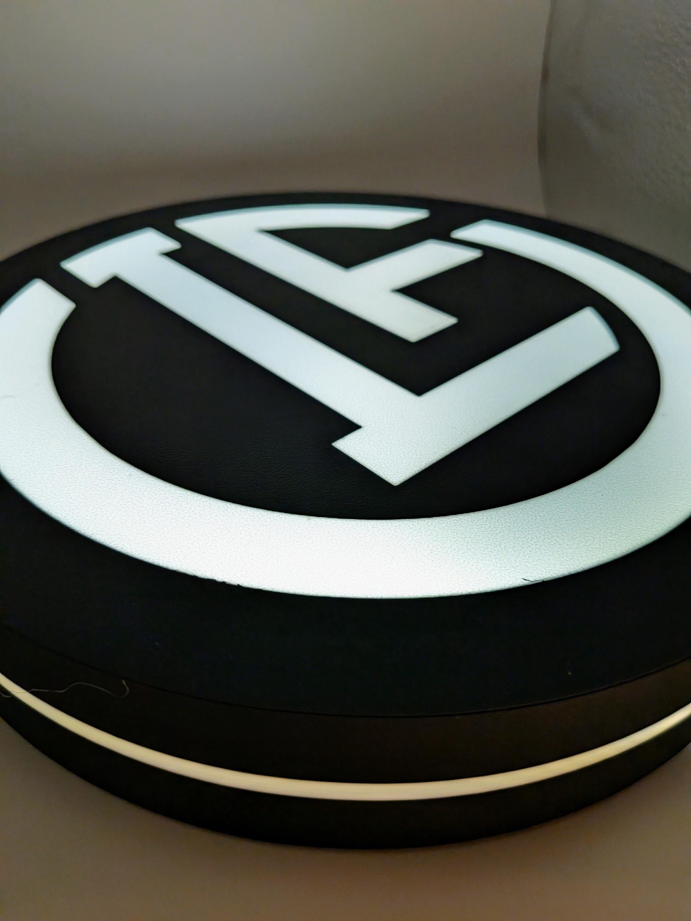 Close-up of lit round LED logo lightbox with white emblem on dark base