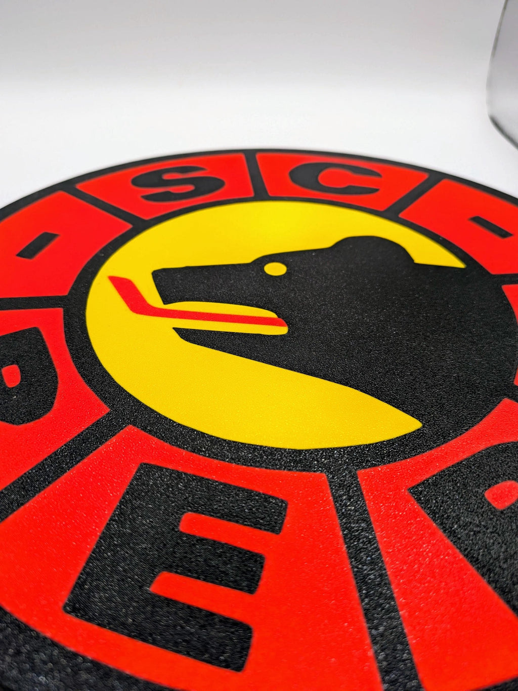 Lampada LED rotonda SC Bern, primo piano del logo: testa nera su cerchio giallo.