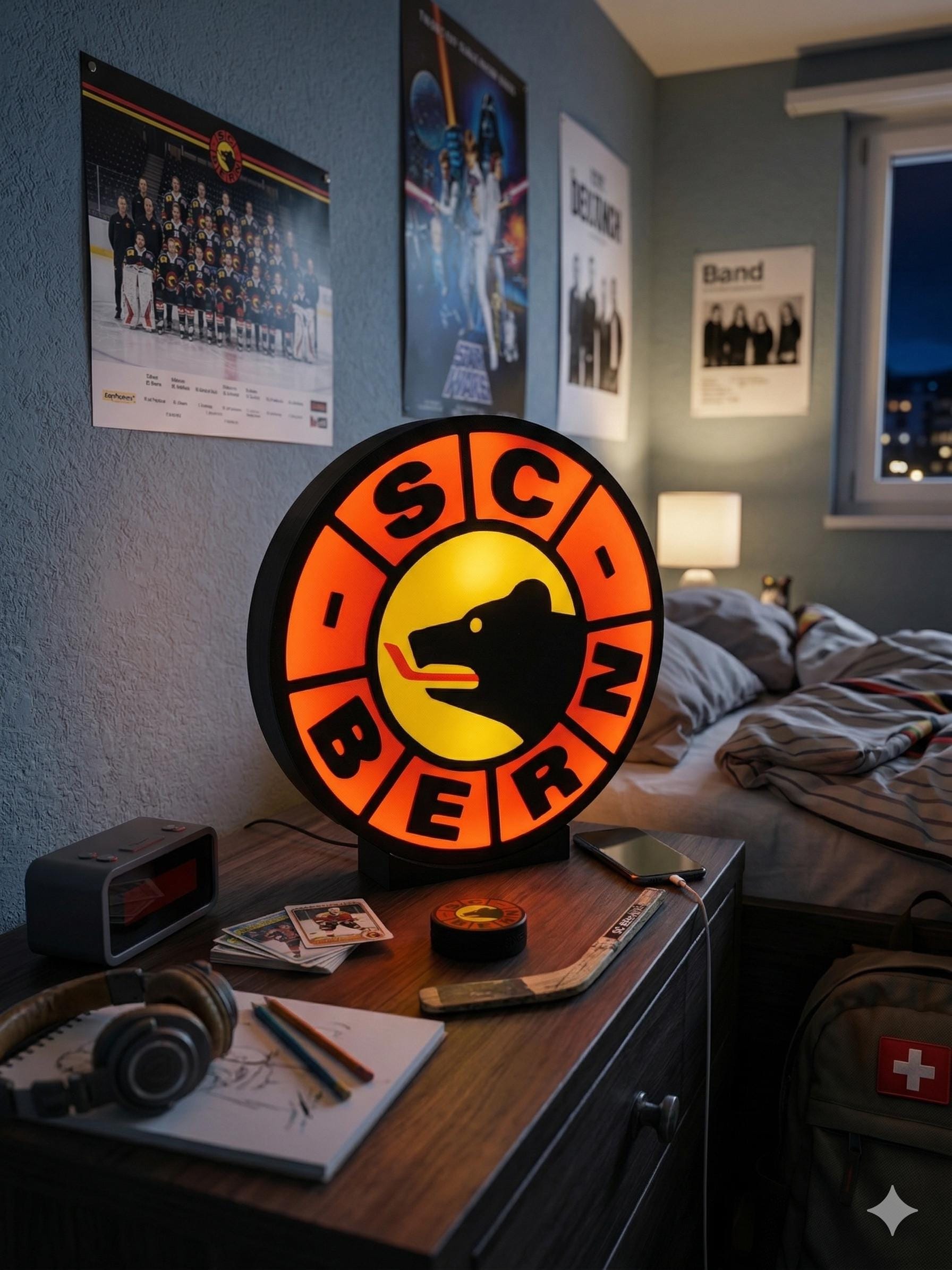 Lampada LED rotonda SC Bern su supporto nero, logo arancione e cerchio giallo accesa.